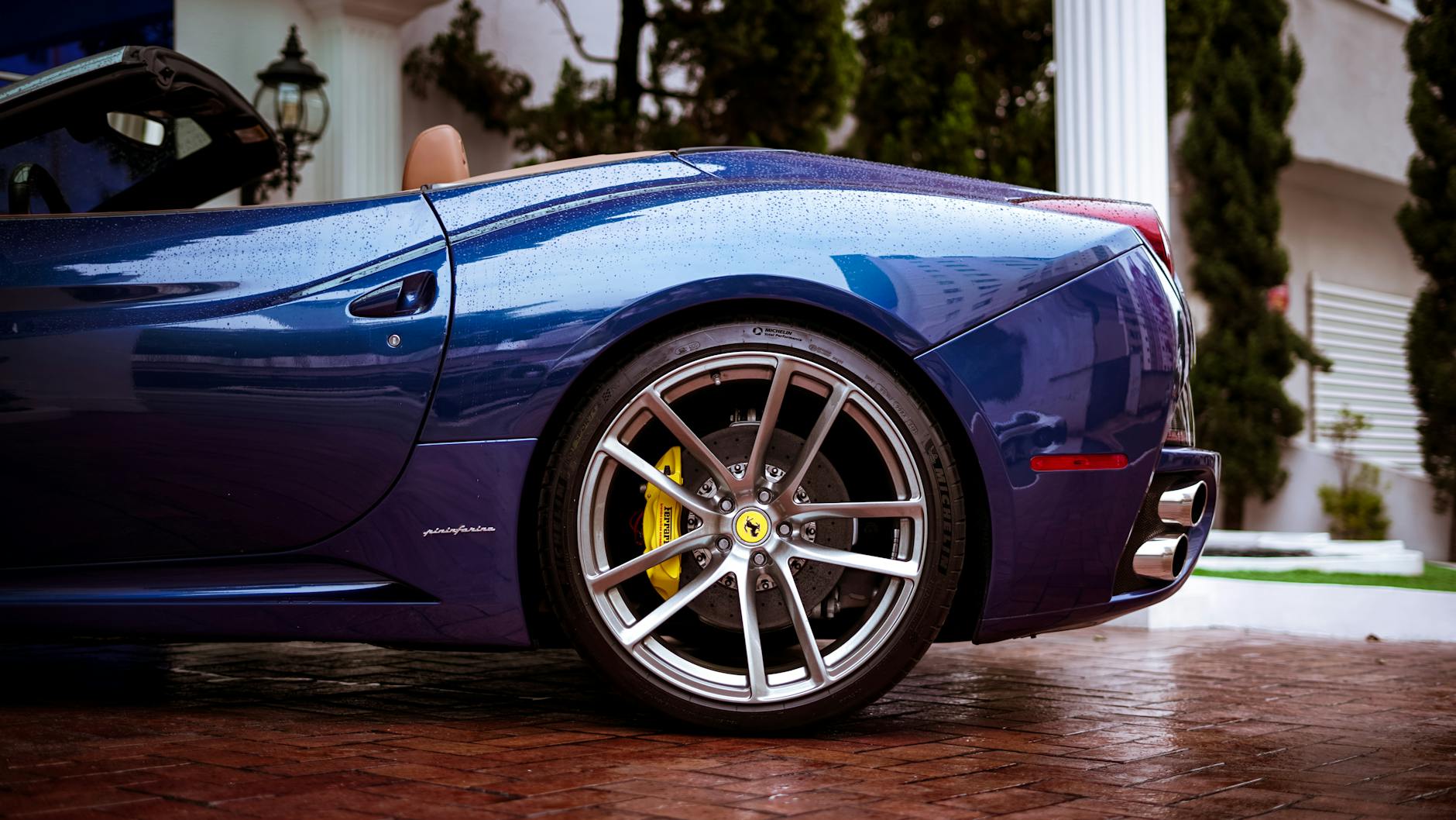 Close-up side view of a blue luxury Ferrari convertible with raindrops on the surface.