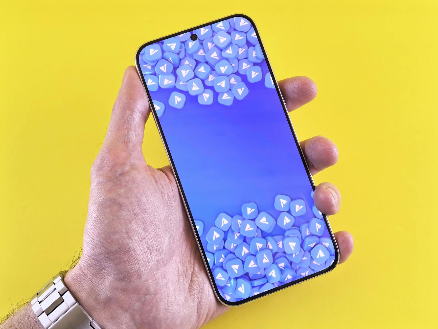 Smartphone displaying social media icons, held in a hand against a bright yellow background.