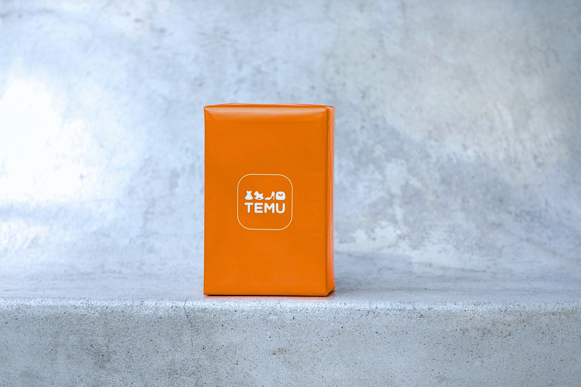 Bright orange parcel with Temu logo on a concrete surface, suitable for ecommerce themes.