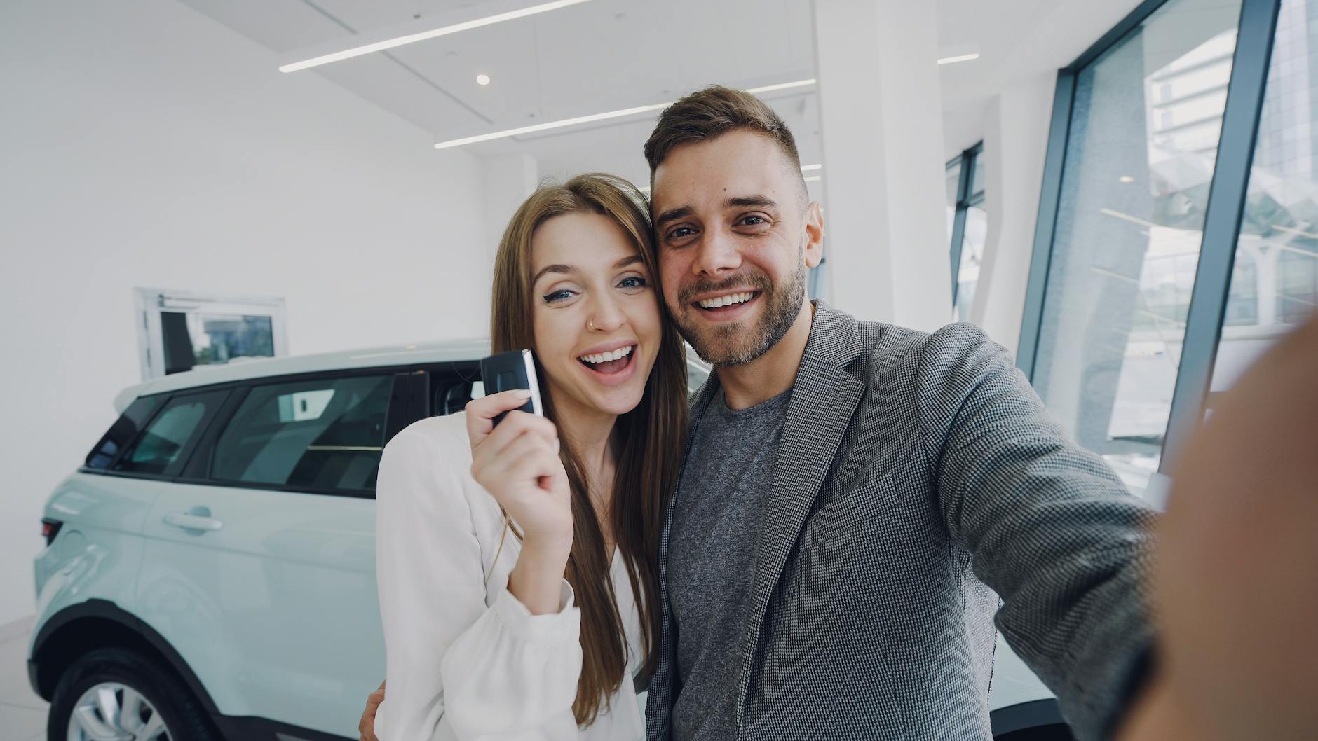 A joyful couple taking a selfie after purchasing a new car, indoors.