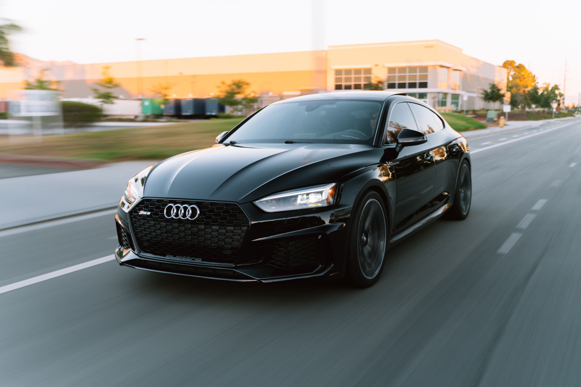 A sleek black Audi RS5 in motion on a city road during daytime.