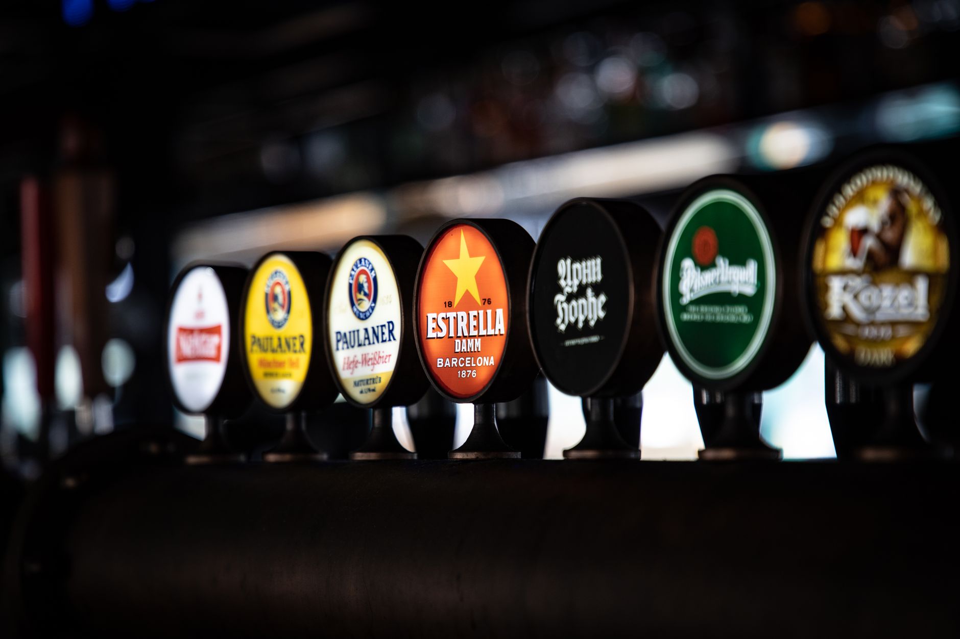 A close-up of various beer taps in a dimly lit bar, showcasing popular brands.