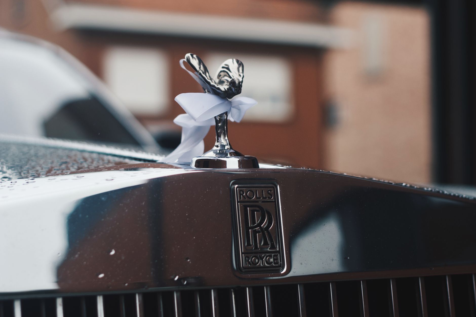 Elegant close-up of a Rolls Royce hood ornament adorned with raindrops. Luxurious and classic automotive design.